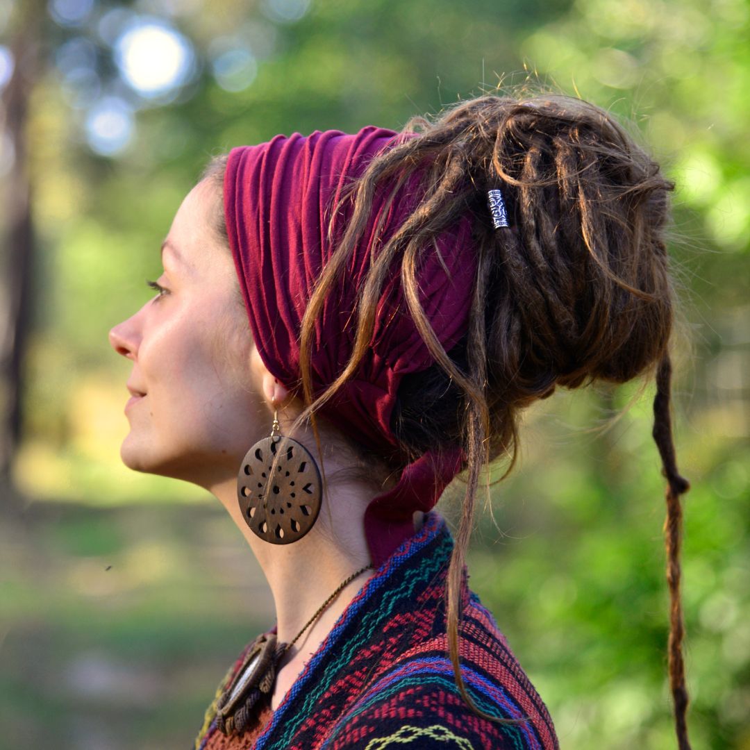 Person with dreadlocks wearing a colorful headscarf and earrings in a natural setting