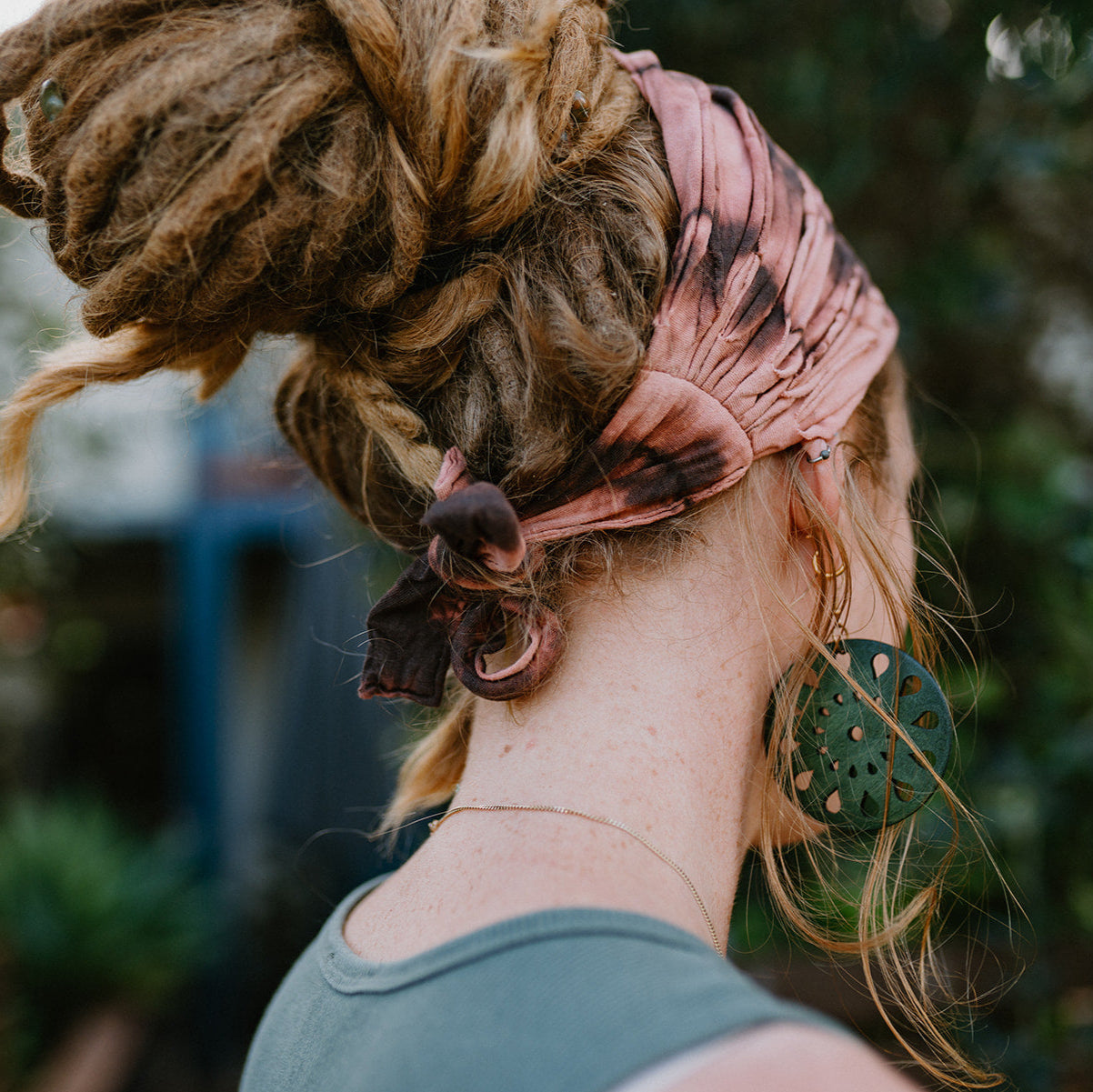 Lady with dreads with a brown cotton tie p headband and large earrings.