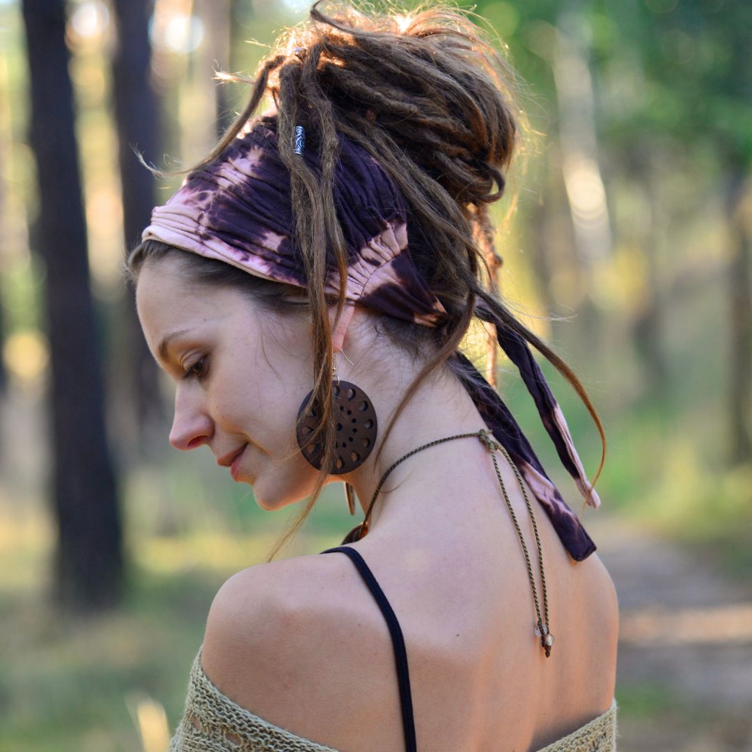 Woman with dreadlocks wearing a headband and earrings in a forest setting