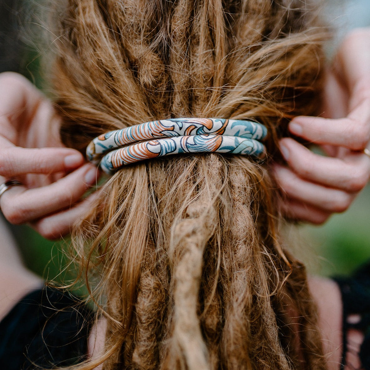 A spiral-shaped dreadlock tie, a spiralock, with a blue and white pattern, placed on a ladies dreadlocks.