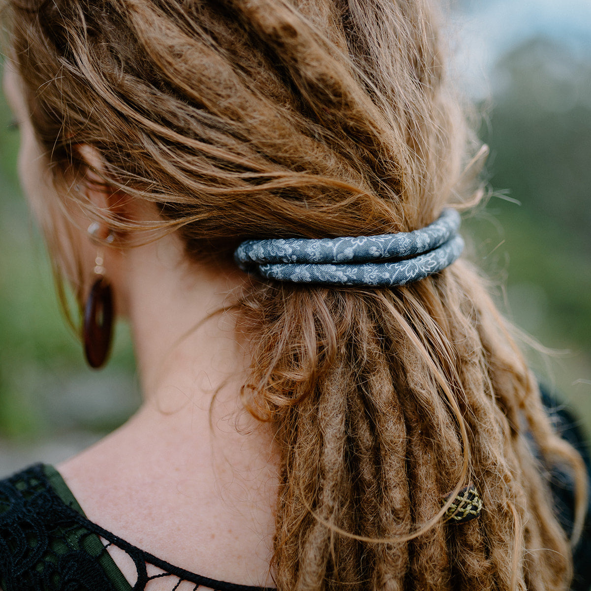 Person with dreadlocks wearing a grey Spiralock hair tie against a blurred natural background