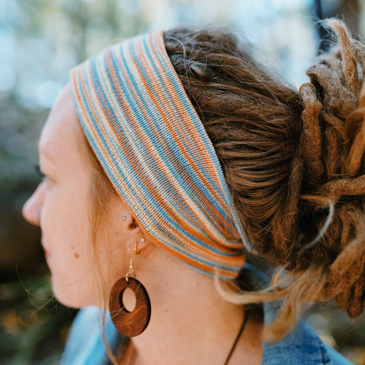 Person with dreadlocks wearing a striped headband and wooden earrings outdoors