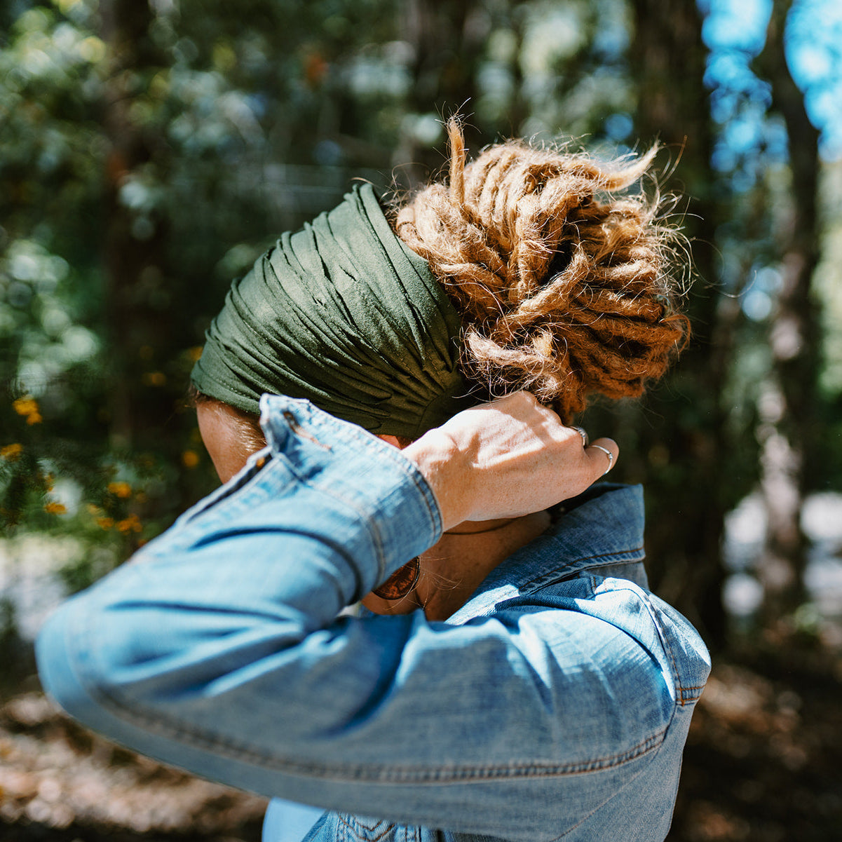 Person wearing a green headscarf and denim jacket in a forest setting