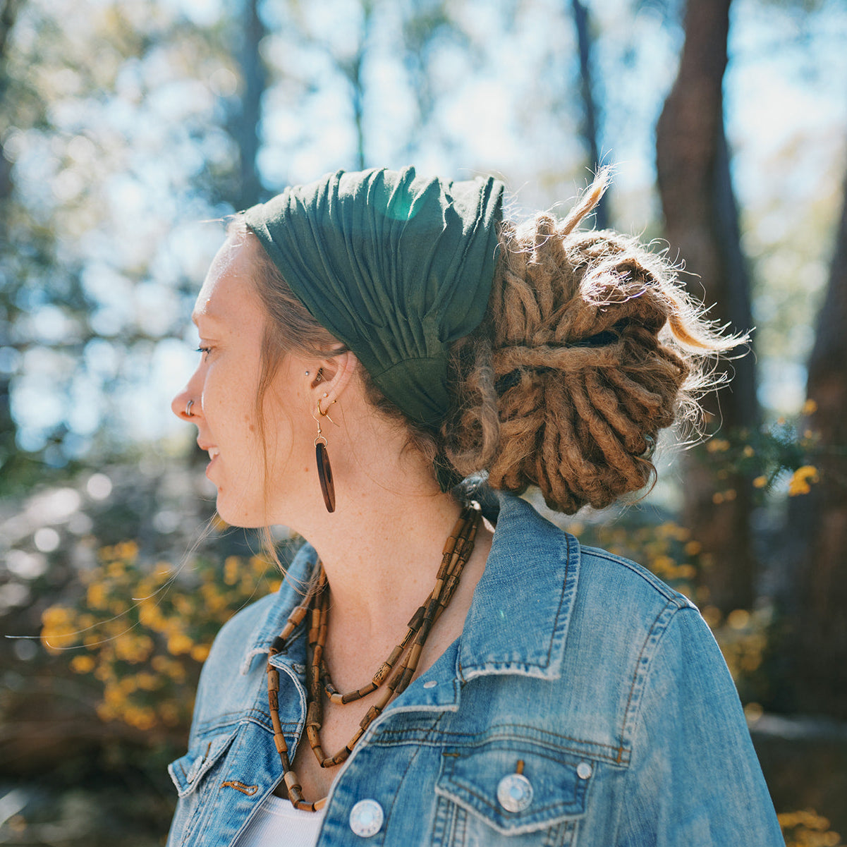 Person with dreadlocks in a natural setting with trees and flowers.