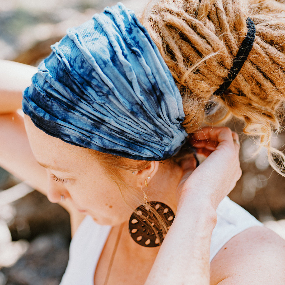 Person with blue headband and earrings adjusting hair outdoors
