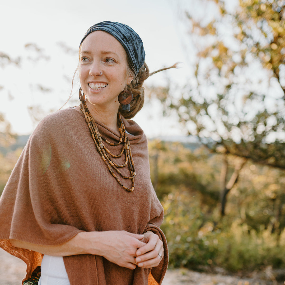 Woman wearing a brown poncho and blue headscarf in a natural setting