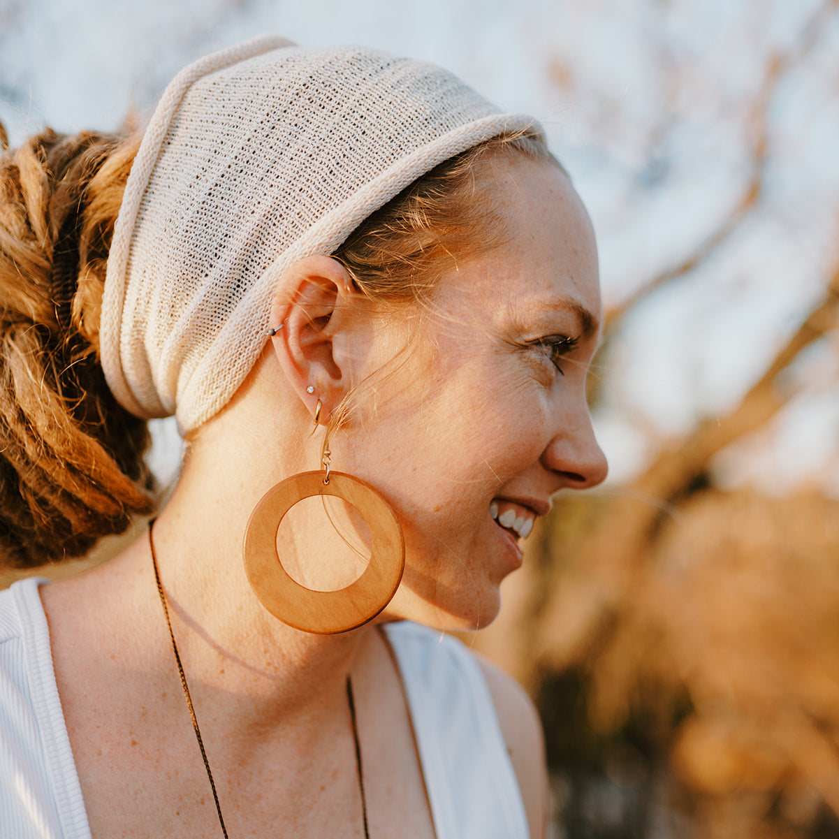 Woman wearing a beige headband and wooden earrings outdoors
