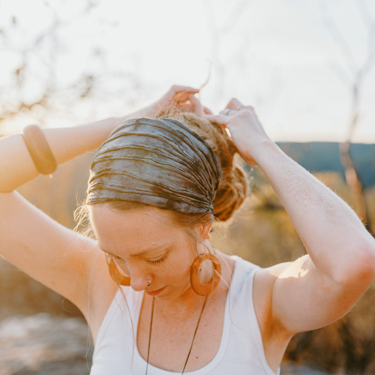 Woman tying her hair in a bun outdoors with a blurred natural background