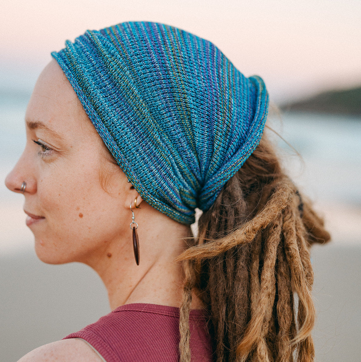 Woman with dreadlocks wearing a blue headband against a blurred natural background