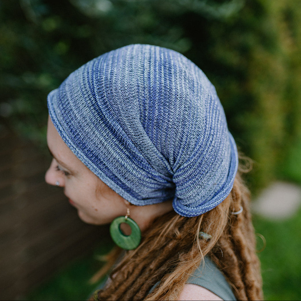 Person wearing a blue knitted headband with green earrings outdoors.