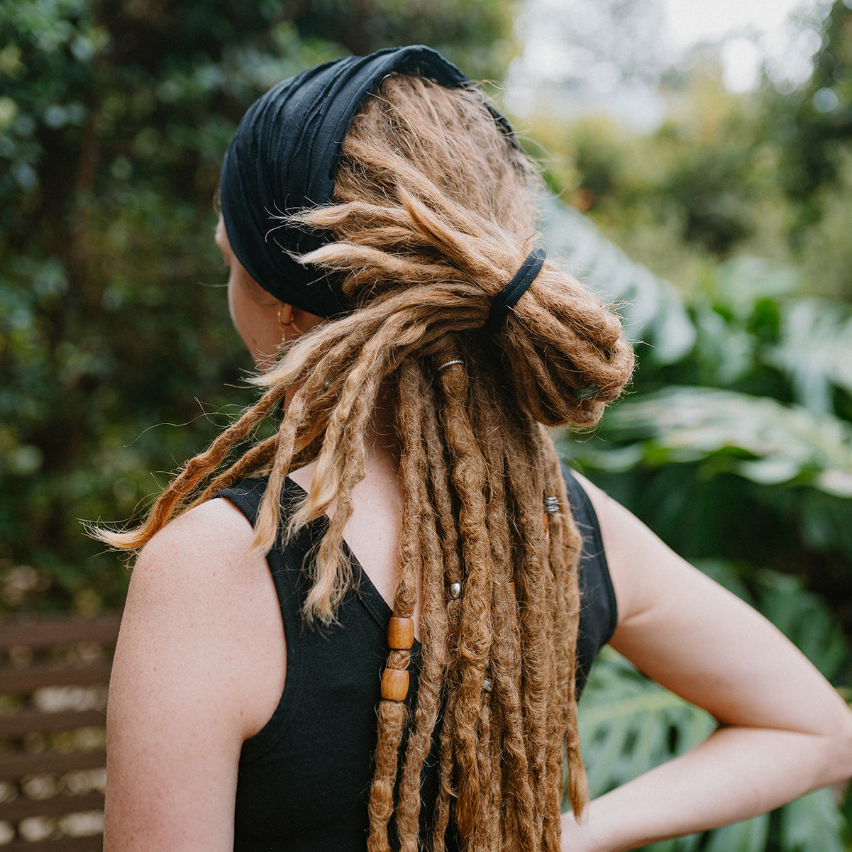Person with long dreadlocked hair wearing a black sleeveless top in a natural setting.