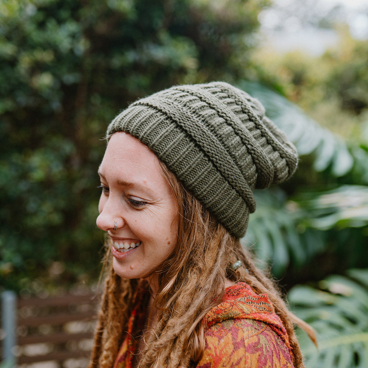 Woman wearing a large green knitted beanie in a natural setting.