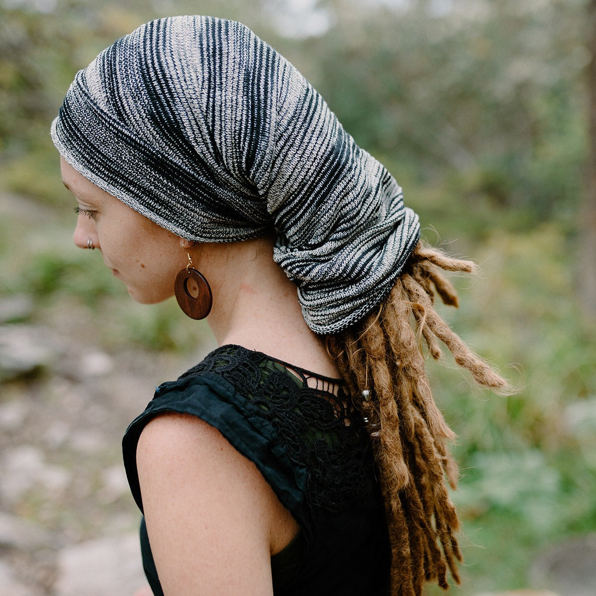 A person wearing a multicolored tube sock headband wrapped around their head with dreadlocks extending from the sides.