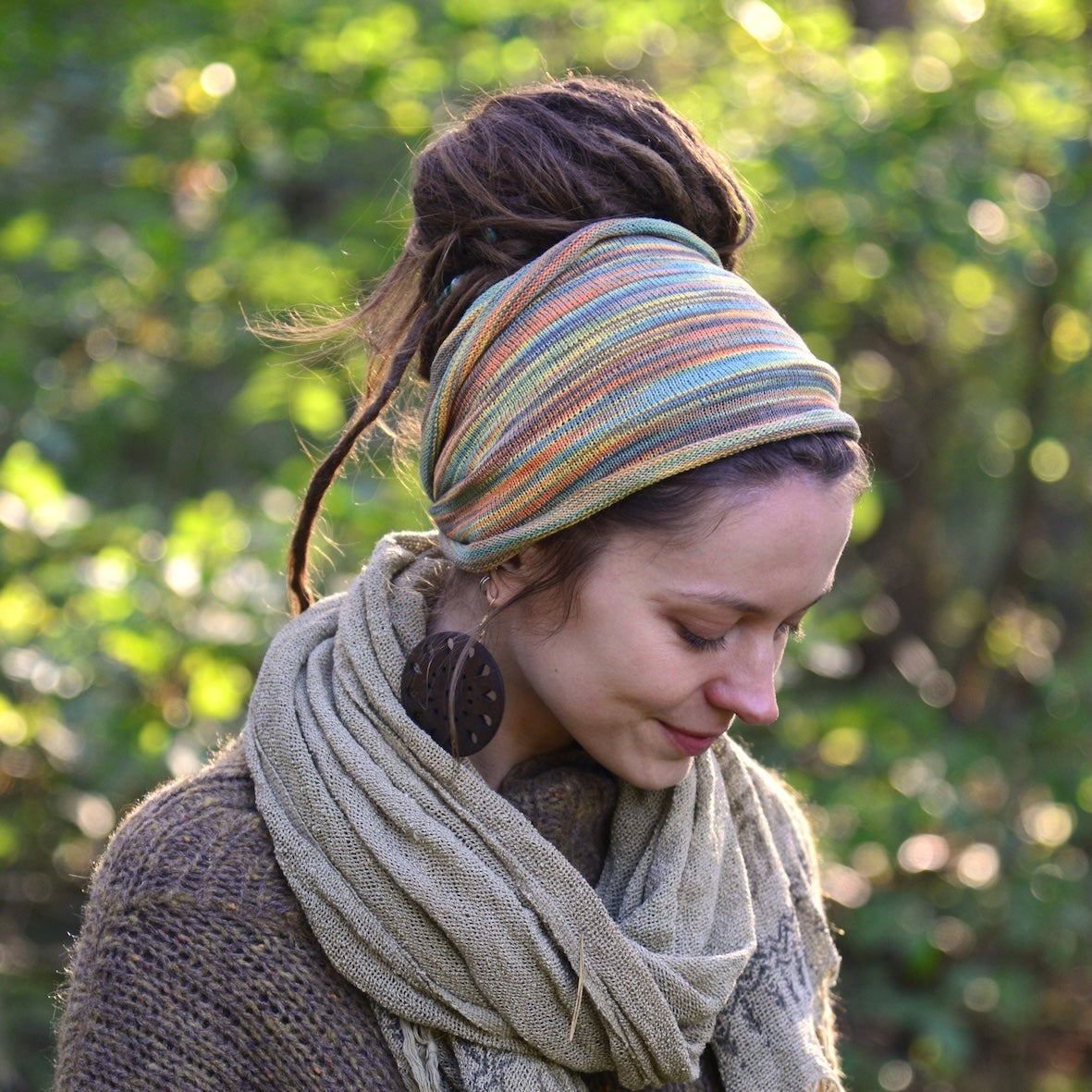 Woman wearing a colorful headband and scarf outdoors with greenery in the background