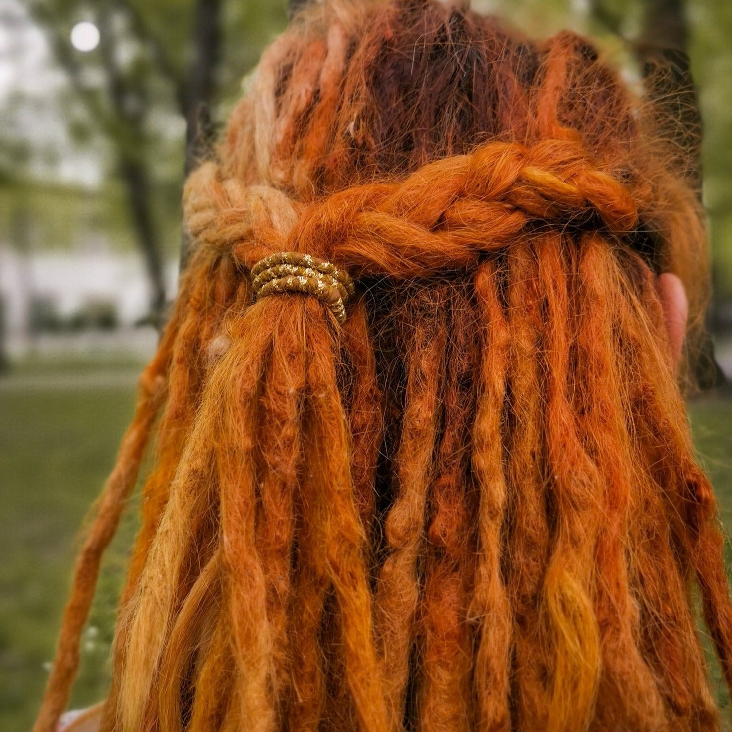 A mini spiral-shaped dreadlock tie, a spiralock, with a brown and gold pattern, placed in dreadlocks.