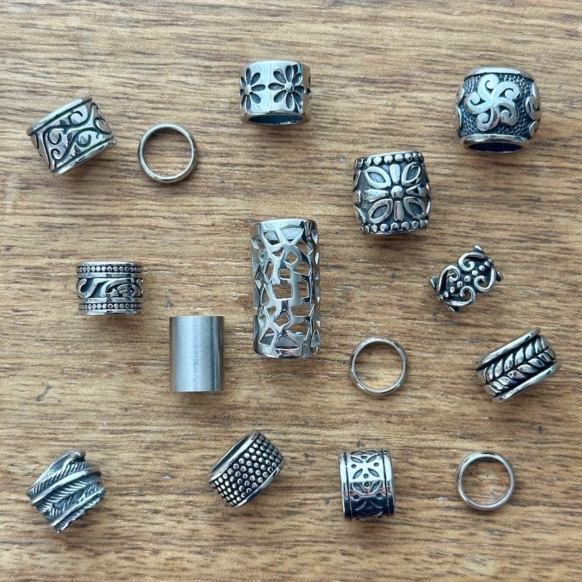 Collection of various stainless steel dreadlock beads and dread rings on a wooden surface
