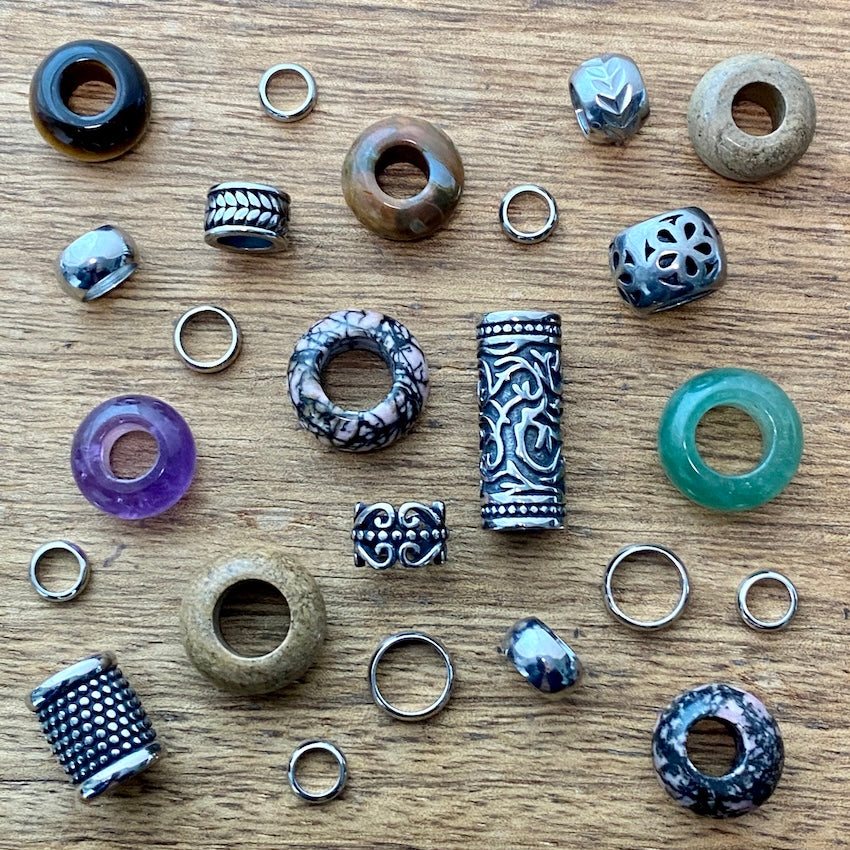 Collection of various dreadlock beads and hair jewellery components on a wooden surface