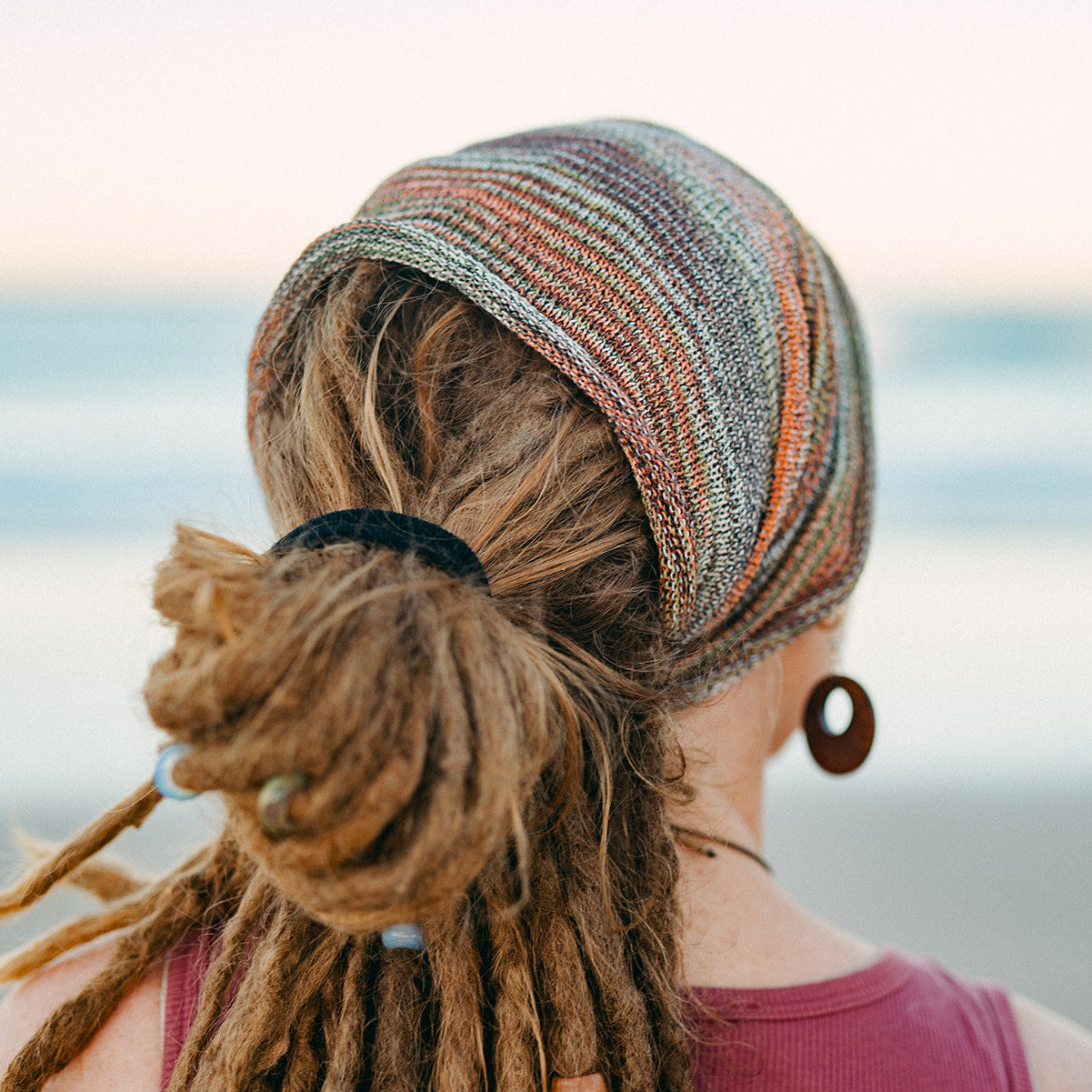 Person with dreadlocks wearing a Earthy coloured headband against a blurred natural background