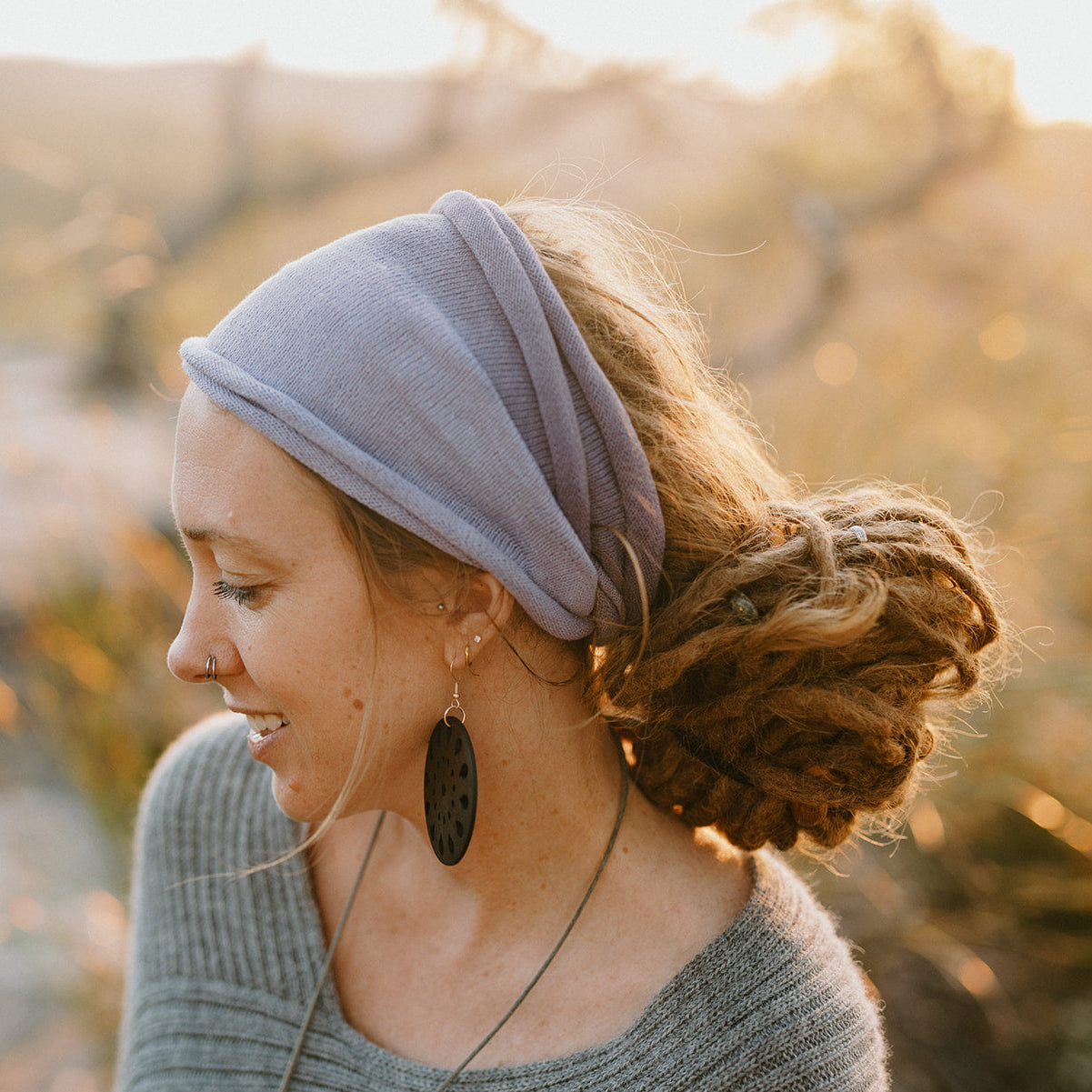Woman wearing a light gray headband and sweater outdoors with a blurred natural background