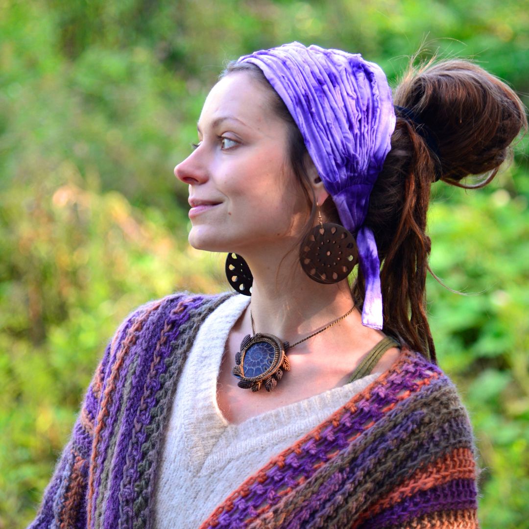 Woman wearing a purple headscarf and colorful cardigan in a natural setting