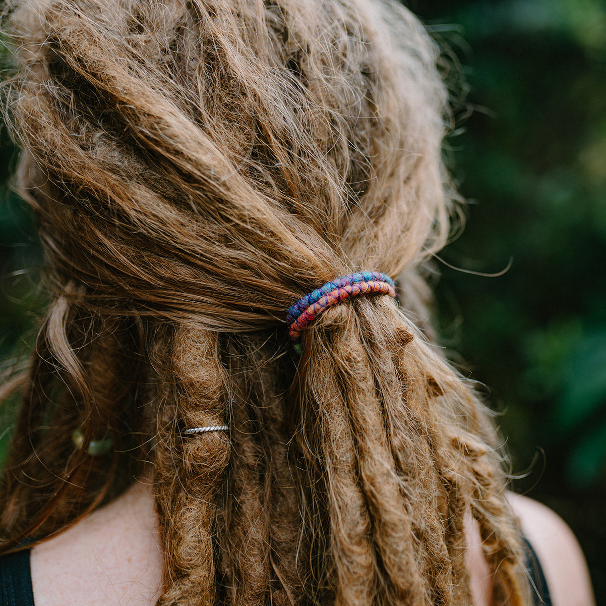 A mini spiral-shaped dreadlock tie, a spiralock, with a blue and red pattern, placed in dreadlocks.