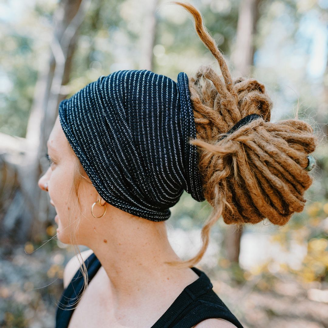 A person wearing a black wide cotton headband with white stripes and dreadlocks.