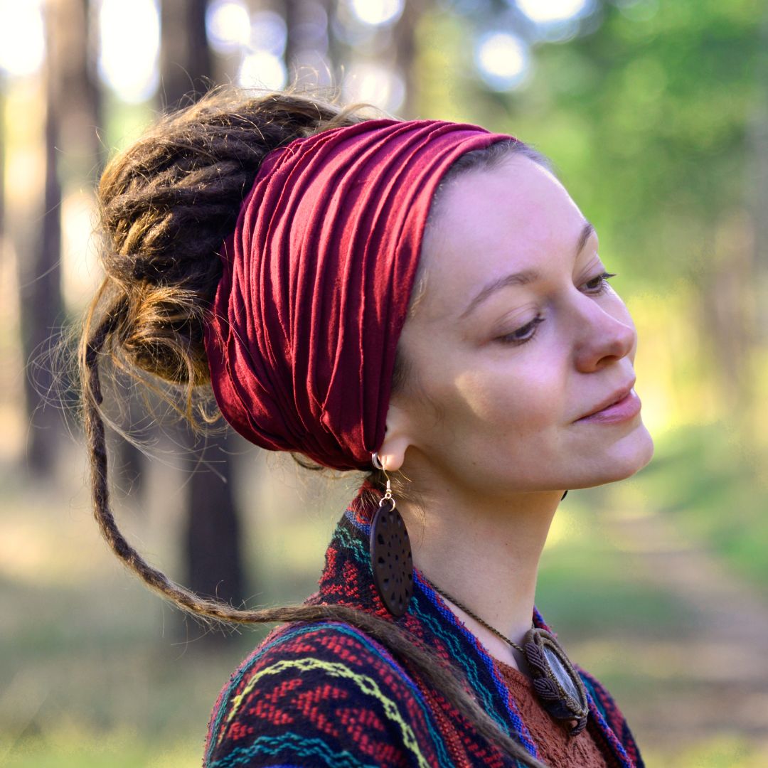 Woman with dreadlocked hair wearing a red headband in a forest setting