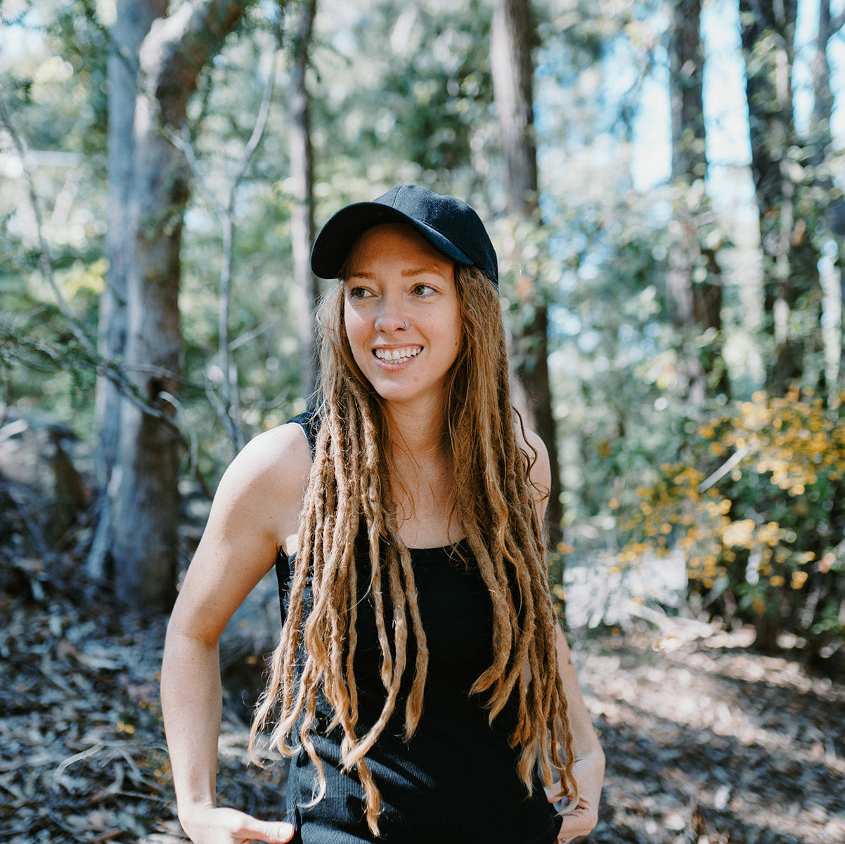 Woman with long braided hair wearing a cap in a forest setting