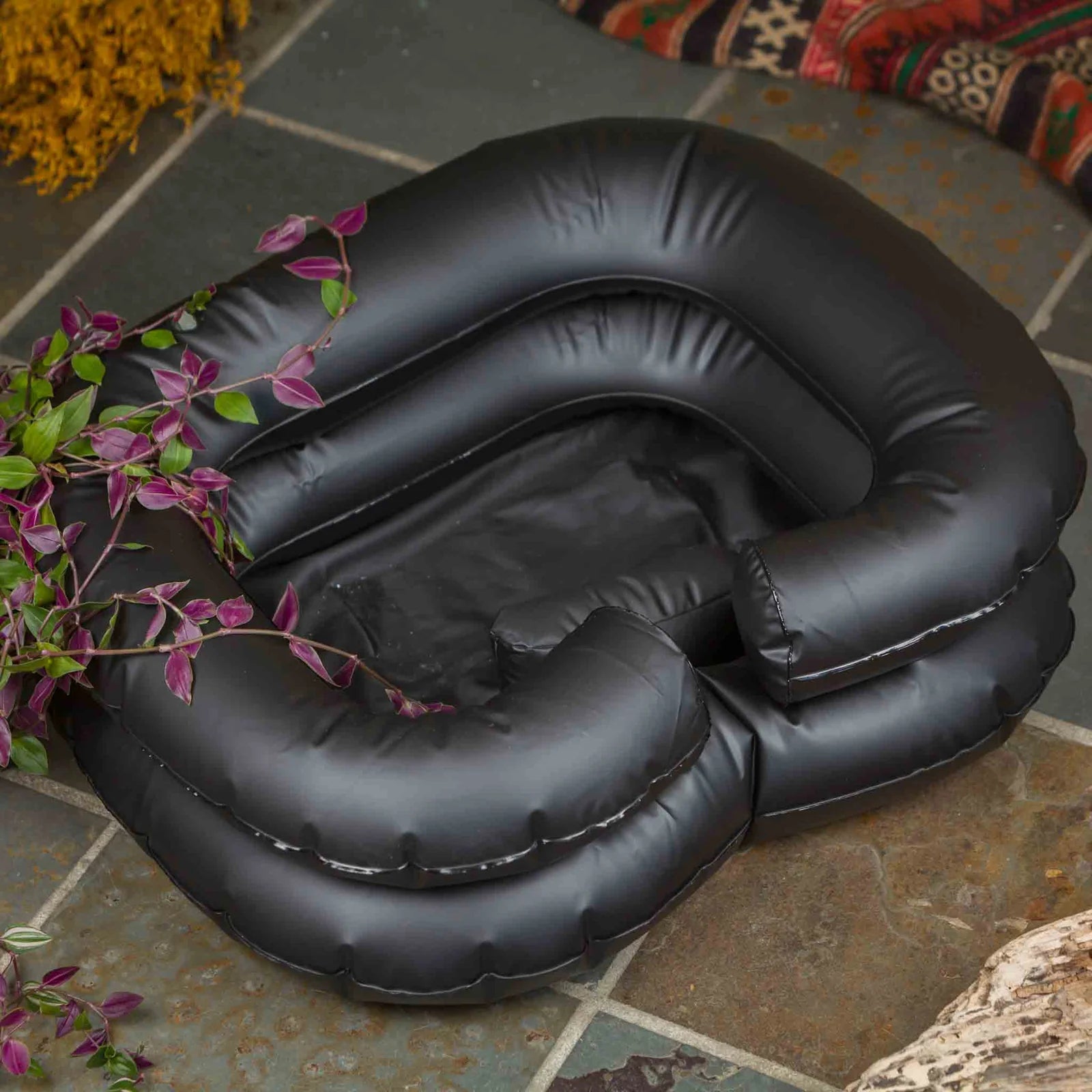 Inflatable black basin designed for dreadlock detoxification, placed on a stone surface with a plant beside it.