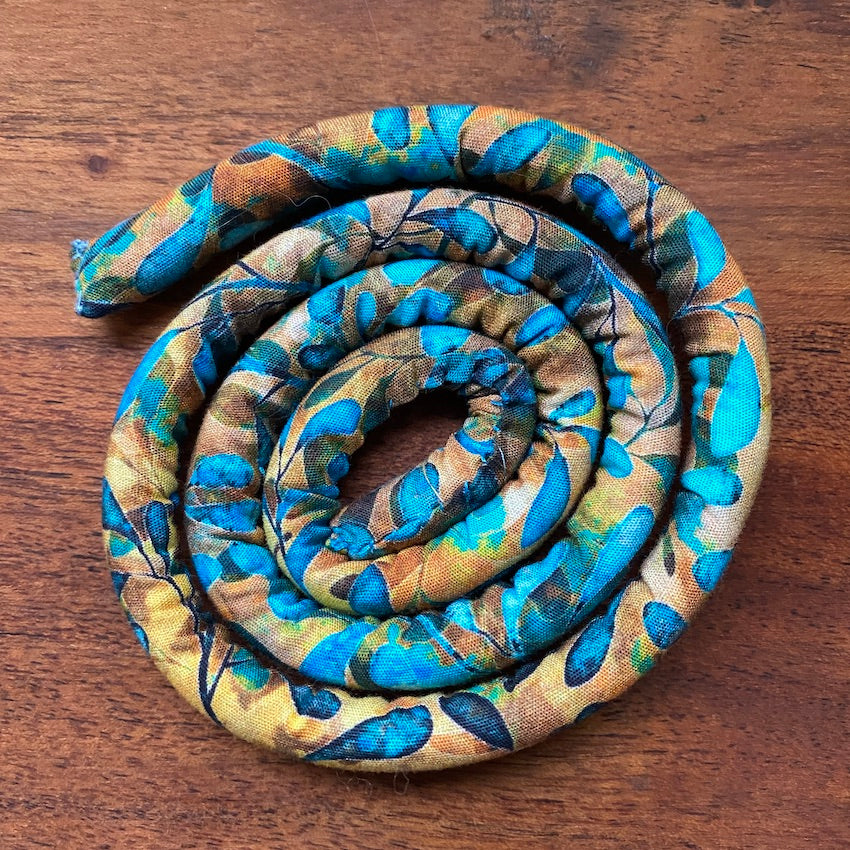 A spiral-shaped dreadlock tie, a spiralock, with a blue and orange pattern, placed on a wooden background.