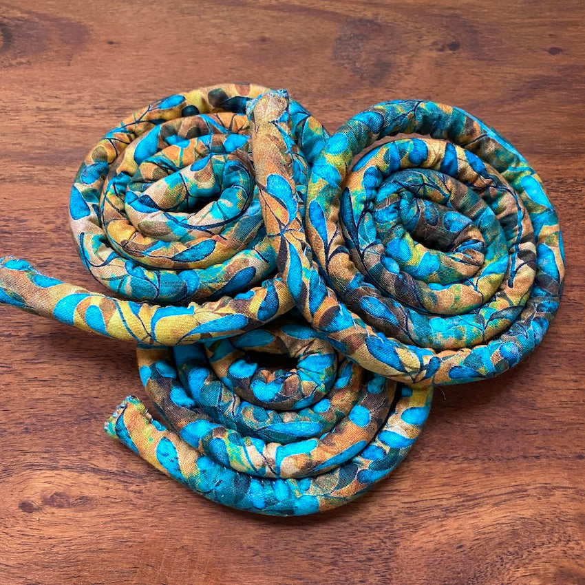 3 spiral-shaped dreadlock ties, a spiralock, with a blue and orange pattern, placed on a wooden background.