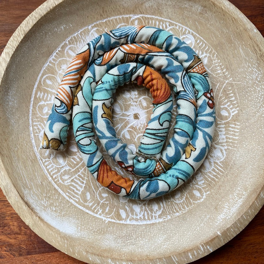 A spiral-shaped dreadlock tie, a spiralock, with a blue and white pattern, placed on a wood surface.
