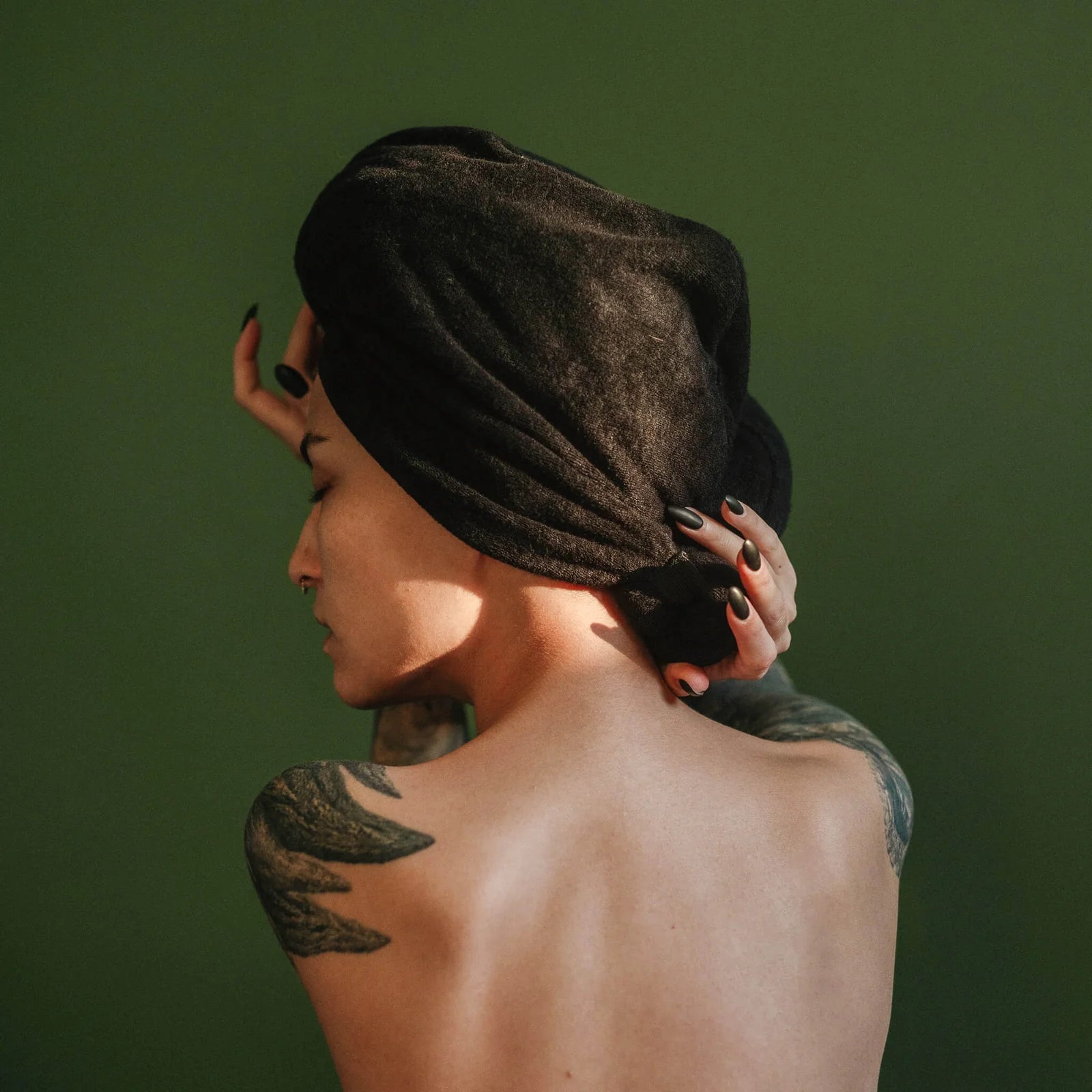 Person with a black Hair Towel and tattoos on a green background
