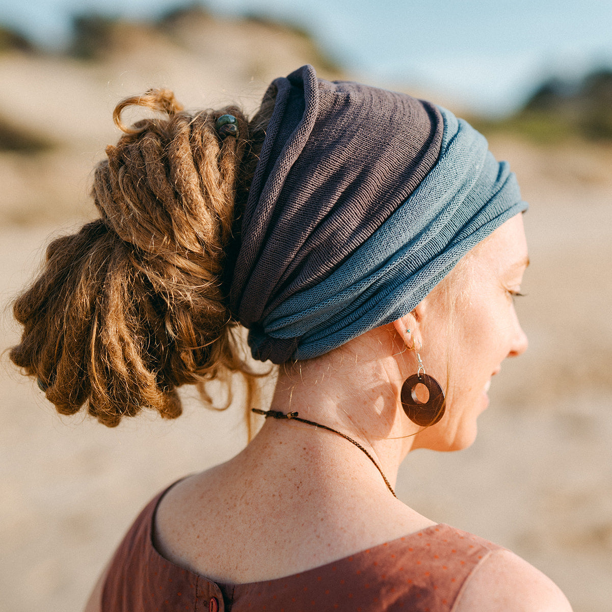Person with dreadlocks wearing a Blue and Brown headband on a beach