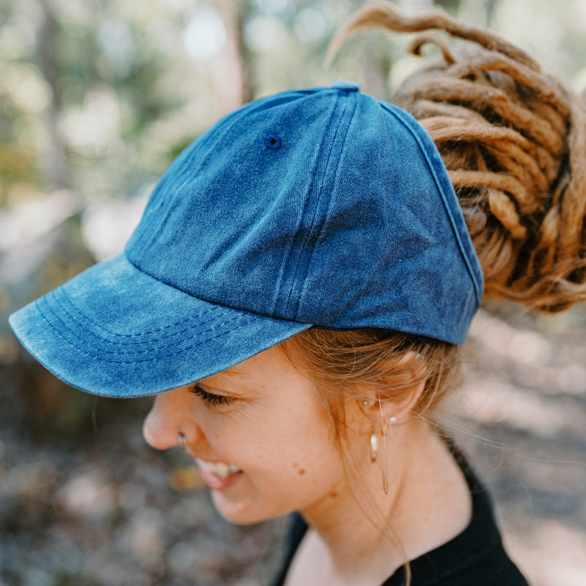 Person wearing a blue open back cap with a blurred natural background