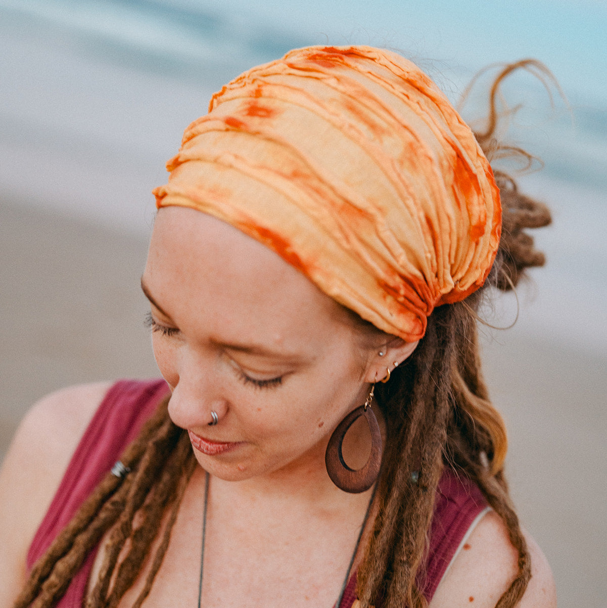 Woman with orange headscarf and dreadlocks against a blurred beach background