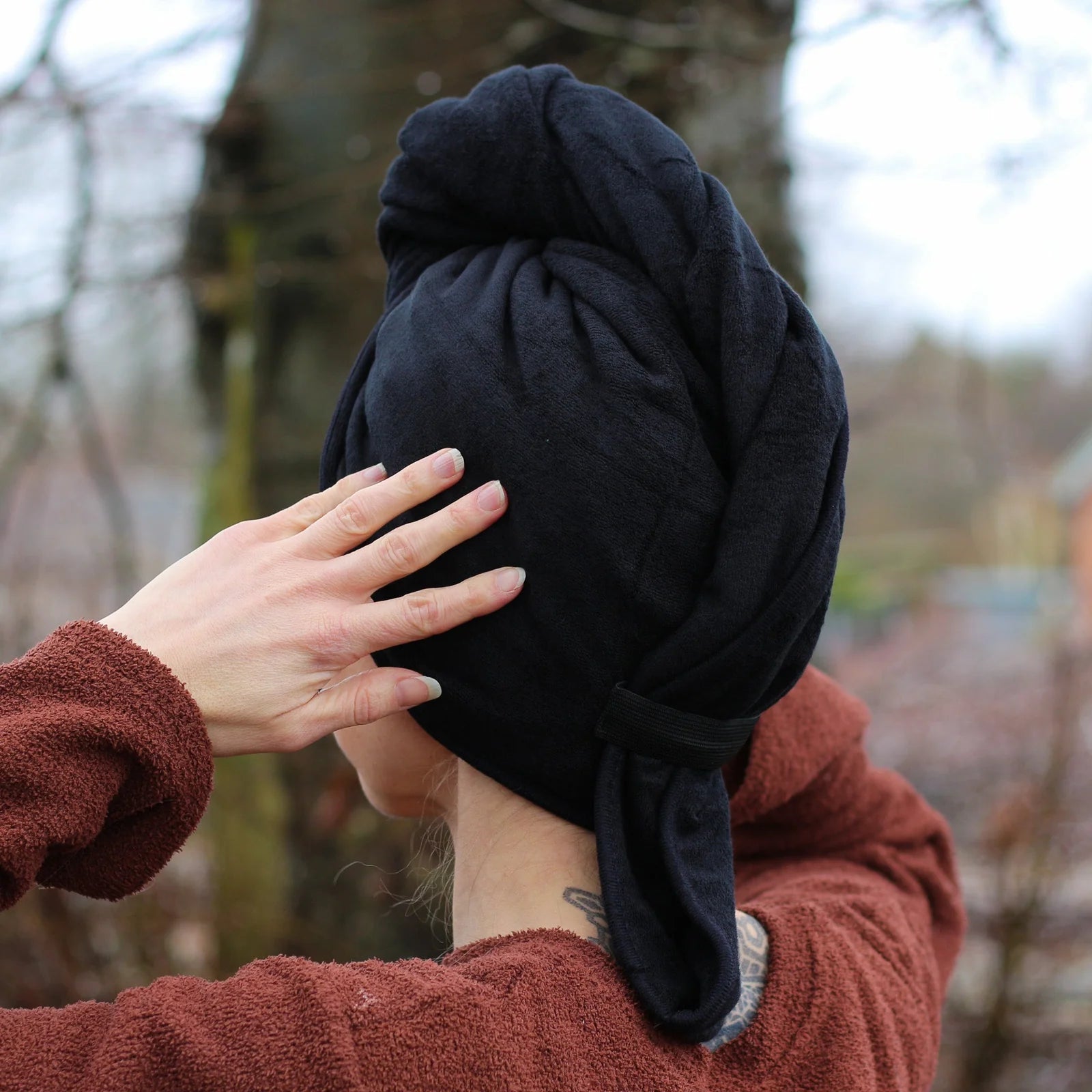 Person wearing a black hair towel with a blurred outdoor background