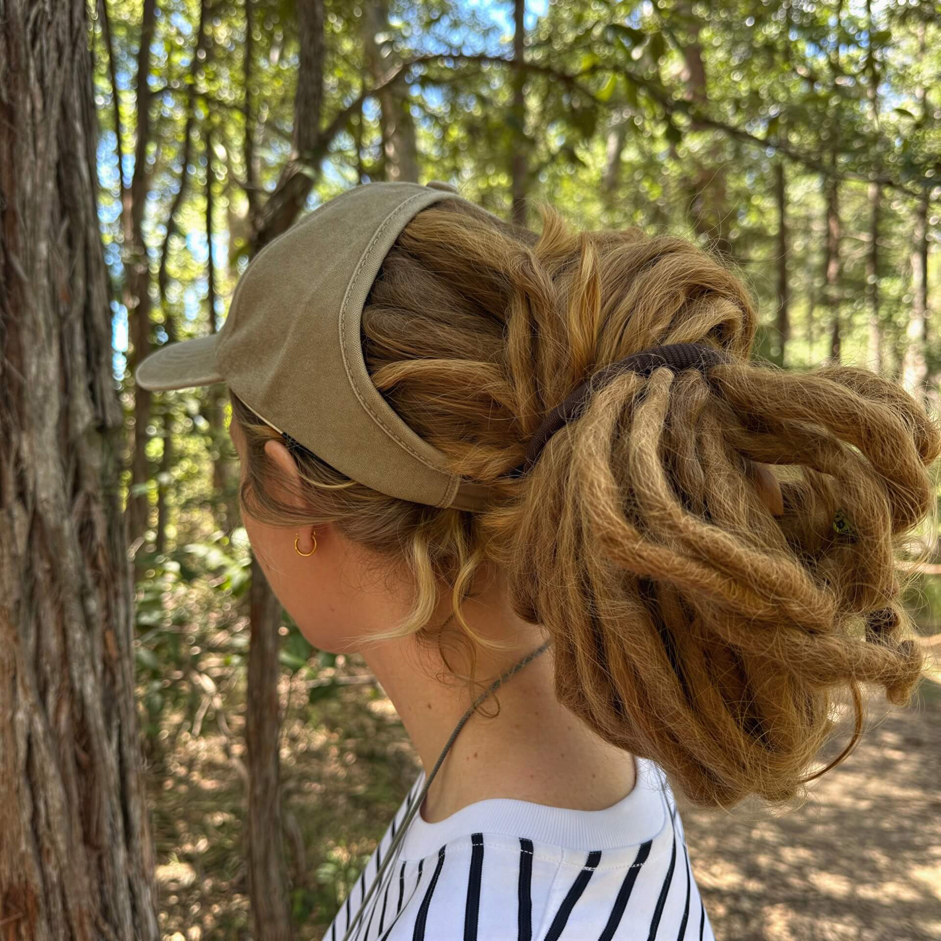 Person with braided hair wearing a dreadlock cap in a forest setting