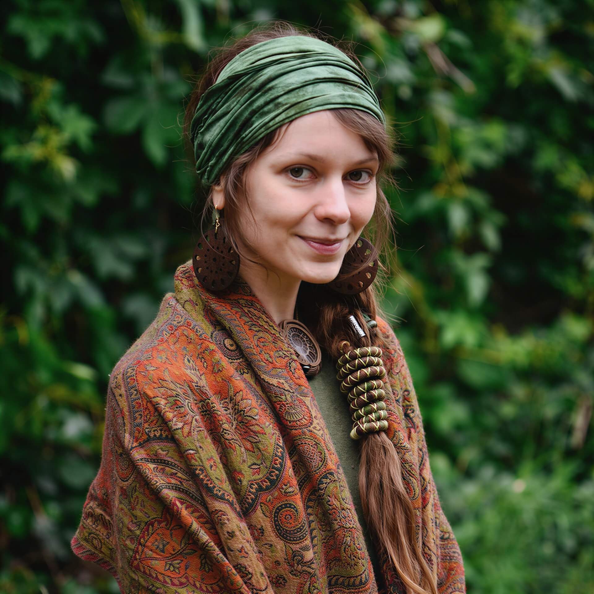 Woman wearing a green headband and patterned scarf against a green leafy background