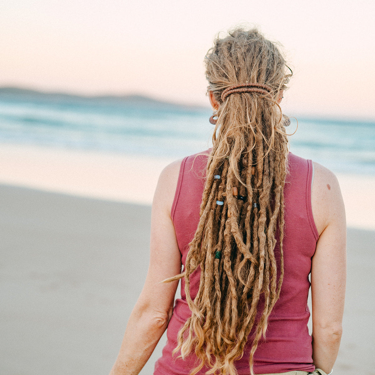 Person with long dreadlocks standing on a beach wearing a spiralock dreadlock tie.