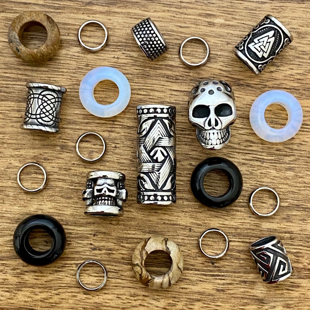 Collection of various dreadlock beads including rings and skull designs on a wooden surface.