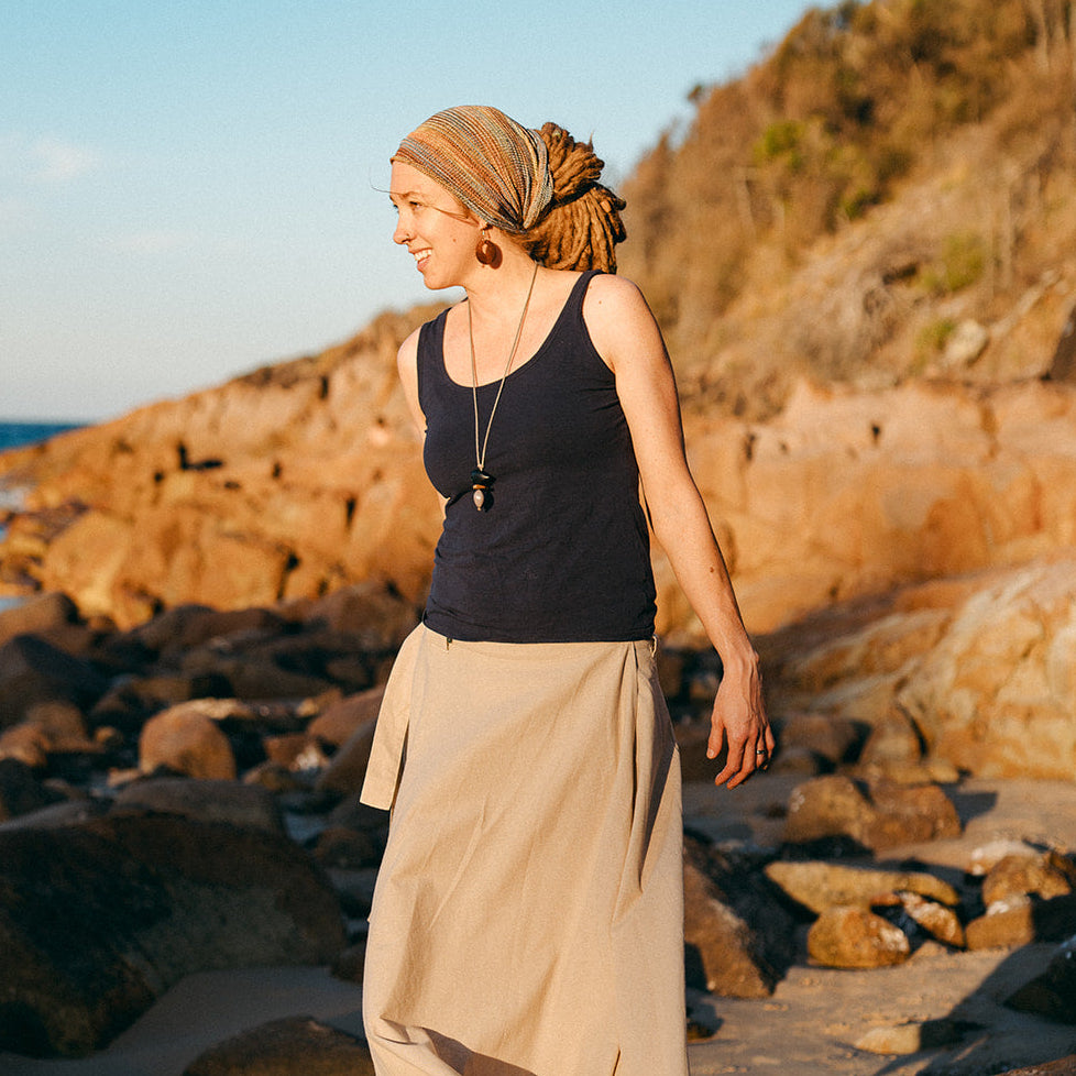 Woman wearing a headband standing on a rocky beach with ocean and cliffs in the background