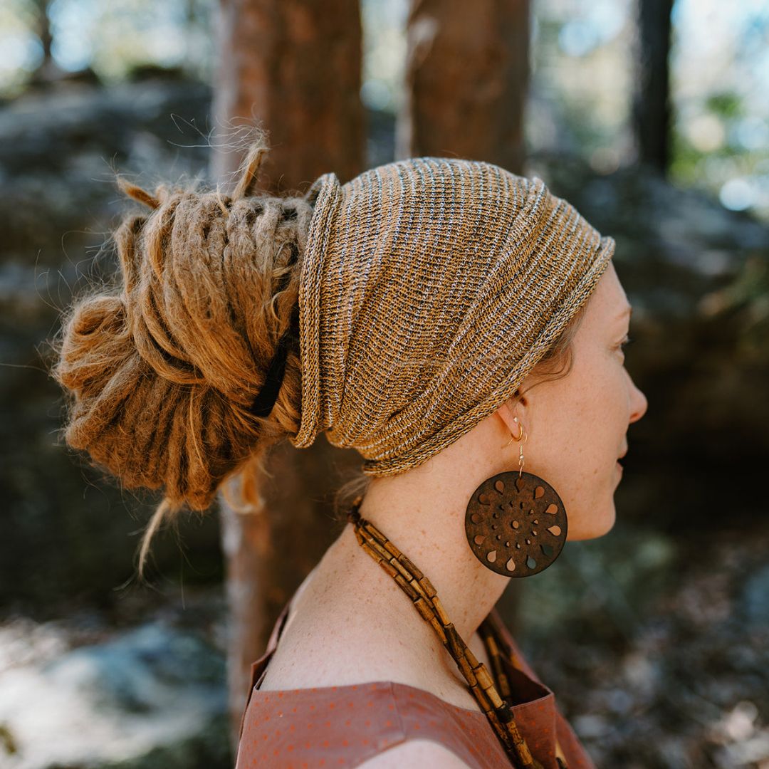 A person wearing a Mustard wide cotton headband and dreadlocks in a blurred bush setting.